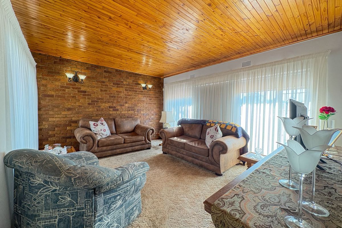 Spacious living room featuring a warm timber ceiling, an exposed brick feature wall, and large windows that provide ample natural light.