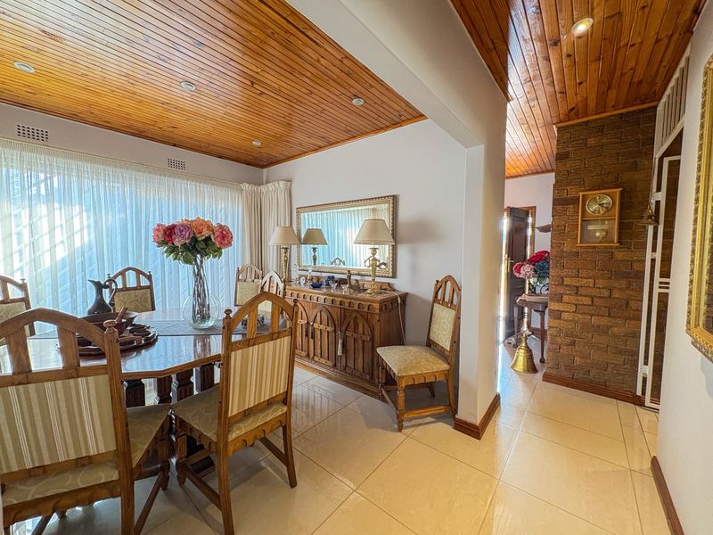 Dining room featuring a warm timber tongue and groove ceiling, tiled flooring, and an exposed brick feature wall leading into the hallway.