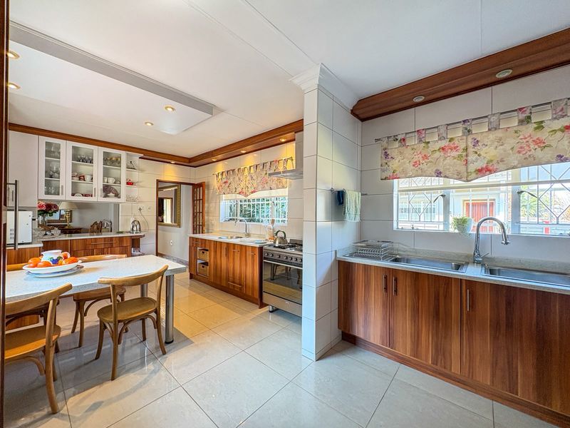 Spacious kitchen featuring warm wood cabinetry, tiled flooring, a gas stove, and a double sink, offering a functional and well-maintained cooking area.