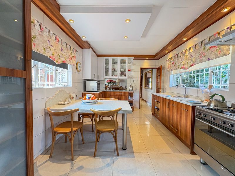 A well-maintained kitchen featuring wood-finish cabinetry, stone countertops, integrated appliances, and a dedicated breakfast nook area with tiled flooring throughout.