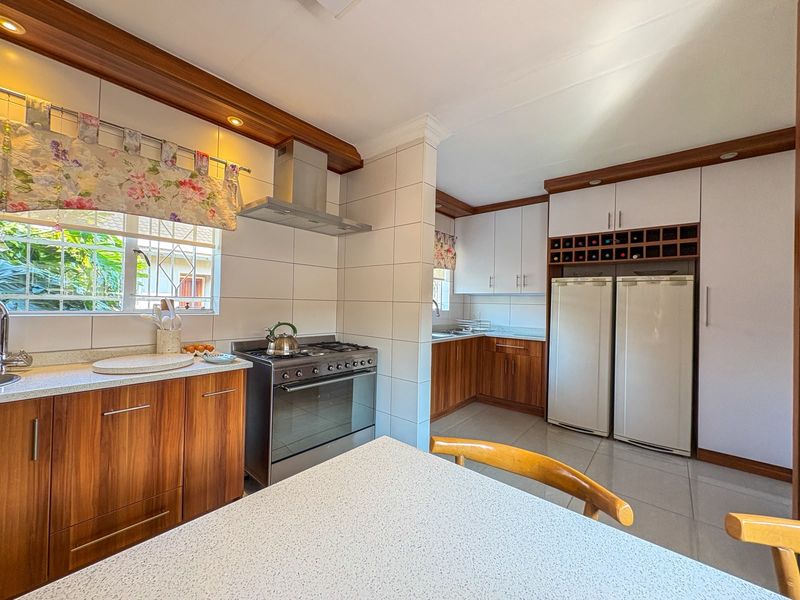 A well-maintained kitchen featuring wood-finish cabinetry, a gas stove with extractor fan, integrated wine storage, and tiled surfaces throughout.