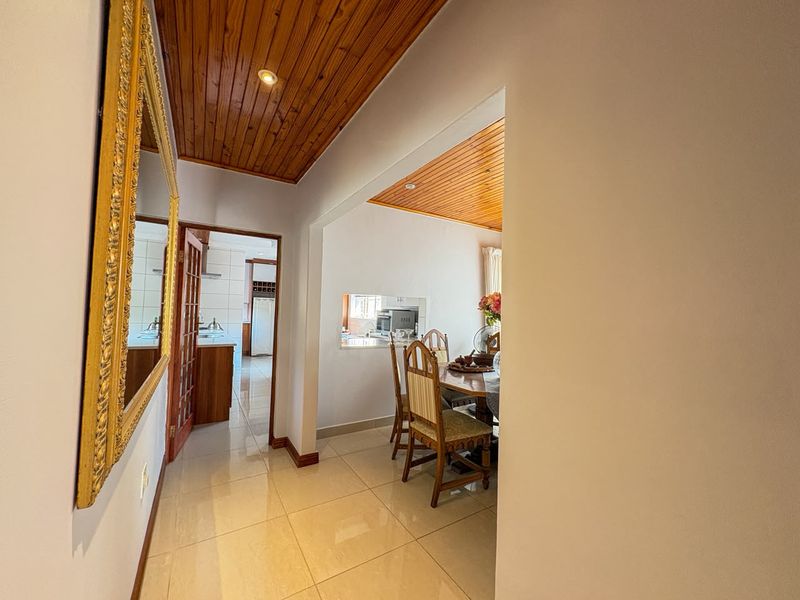 A bright hallway featuring tiled flooring and a timber-paneled ceiling, providing a clear view into the adjacent dining area and kitchen.