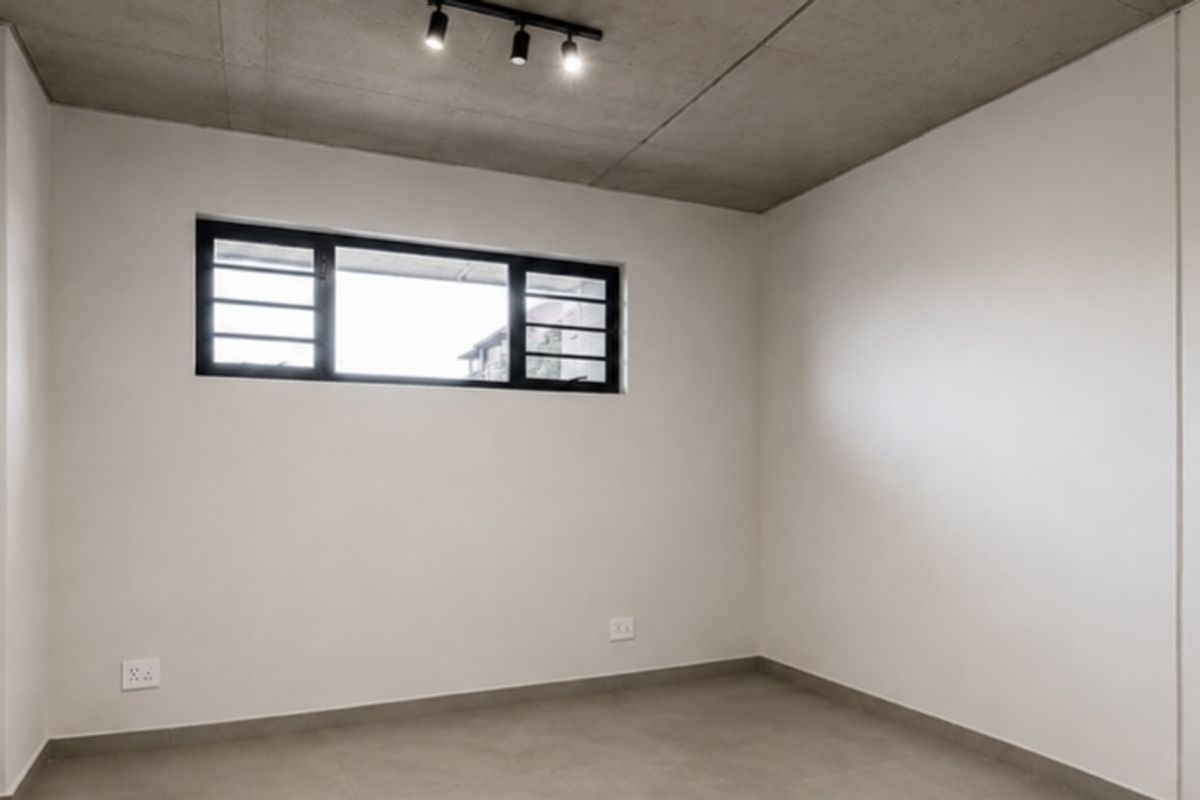A clean, modern bedroom featuring built-in cupboards, an exposed concrete ceiling with track lighting, and neutral tiled flooring.