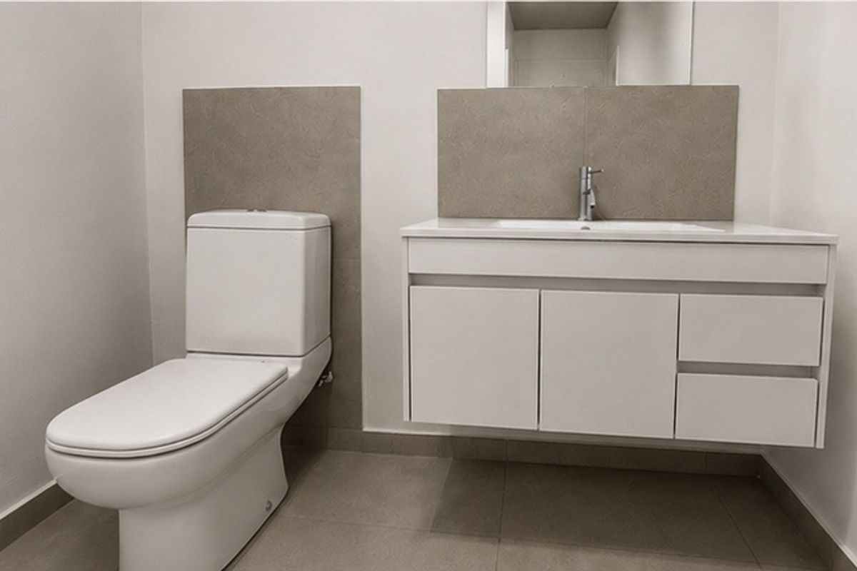 A modern, minimalist bathroom featuring a wall-mounted vanity with integrated basin, chrome fixtures, and neutral-toned tiled splashbacks and flooring.