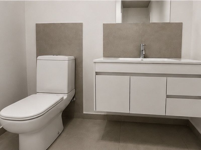 A modern, minimalist bathroom featuring a wall-mounted vanity with integrated basin, chrome fixtures, and neutral-toned tiled splashbacks and flooring.