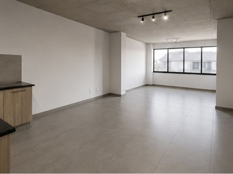 Modern open-plan living area featuring an exposed concrete ceiling, tiled floors, and a compact kitchen with sleek cabinetry and stone countertops.