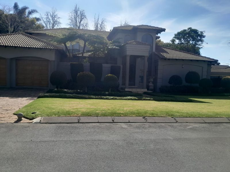 Front elevation of a multi-level residence featuring a tiled roof, double garage, paved driveway, and established garden landscaping.