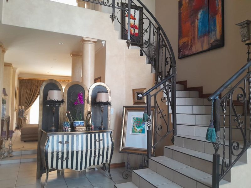 Grand entrance hall featuring a striking wrought iron staircase, tiled flooring, and decorative columns, leading into an open-plan living area.