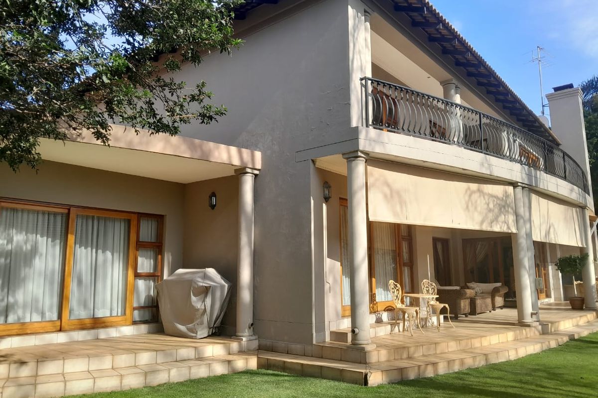 Rear view of the house featuring a spacious tiled patio, upper balcony with wrought iron railing, and classic architectural columns.