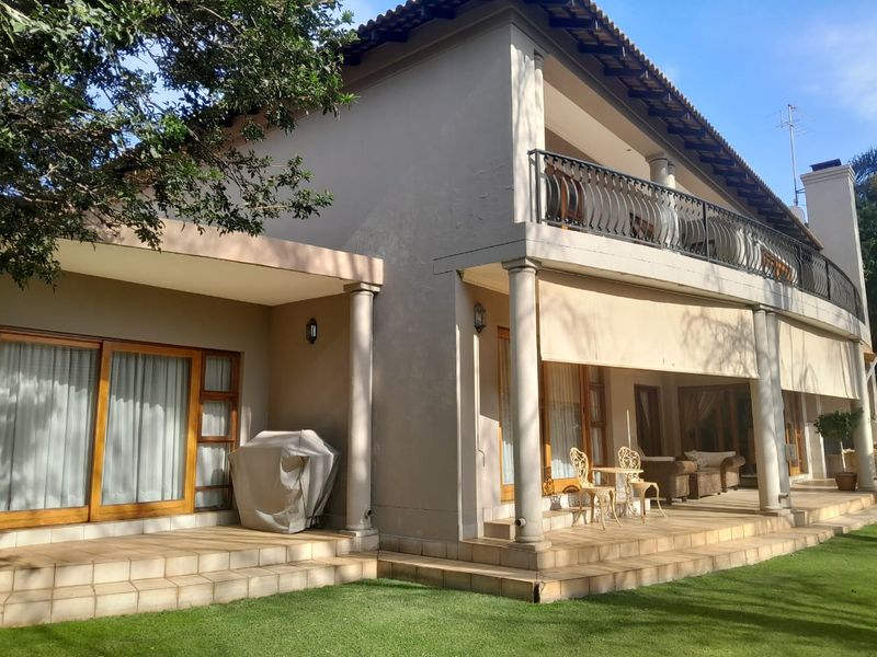 Rear view of the house featuring a spacious tiled patio, upper balcony with wrought iron railing, and classic architectural columns.