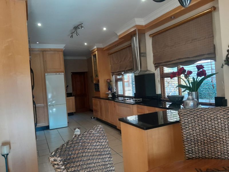 A functional kitchen featuring light wood cabinetry, dark granite countertops, stainless steel extractor fan, and tiled flooring with recessed lighting.