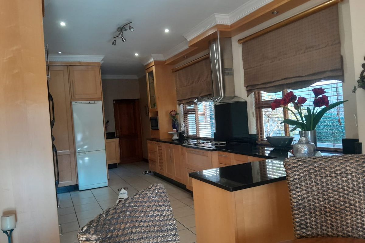 A functional kitchen featuring light wood cabinetry, dark granite countertops, stainless steel extractor fan, and tiled flooring with recessed lighting.