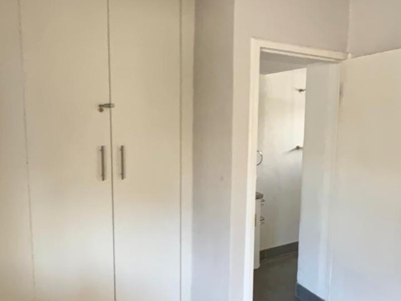 A clean, empty bedroom featuring light-toned laminate flooring, built-in cupboards, and a direct doorway leading to an adjoining bathroom.