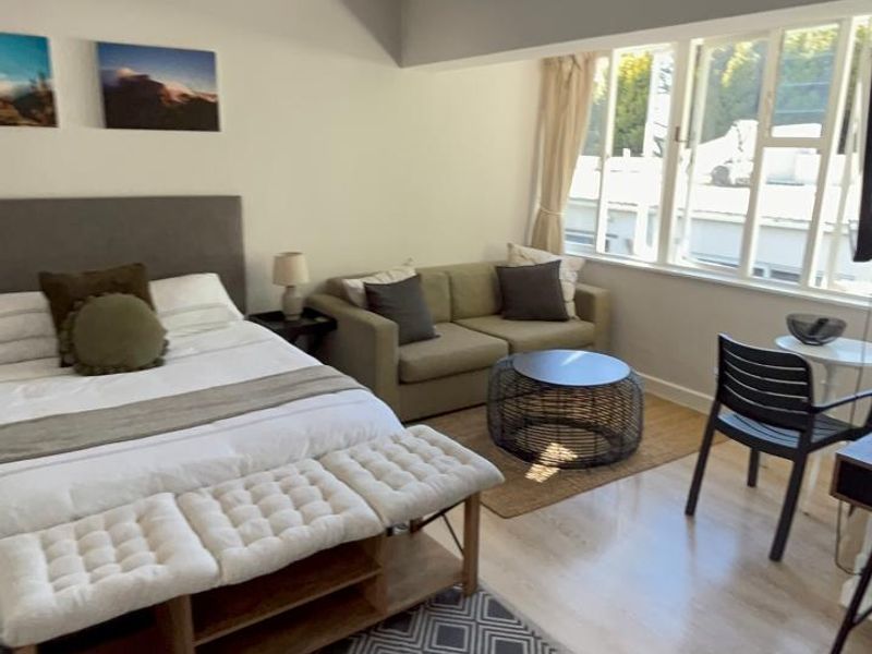 A well-lit bedroom featuring light-toned laminate flooring, neutral wall finishes, and large multi-pane windows providing natural light.