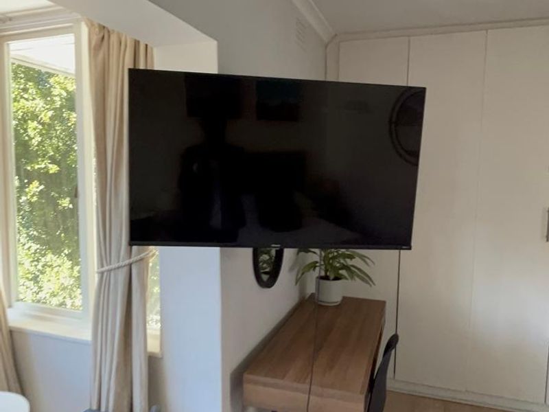 A bedroom featuring built-in wardrobes, laminate flooring, and cove cornicing, with a wall-mounted television and window providing natural light.