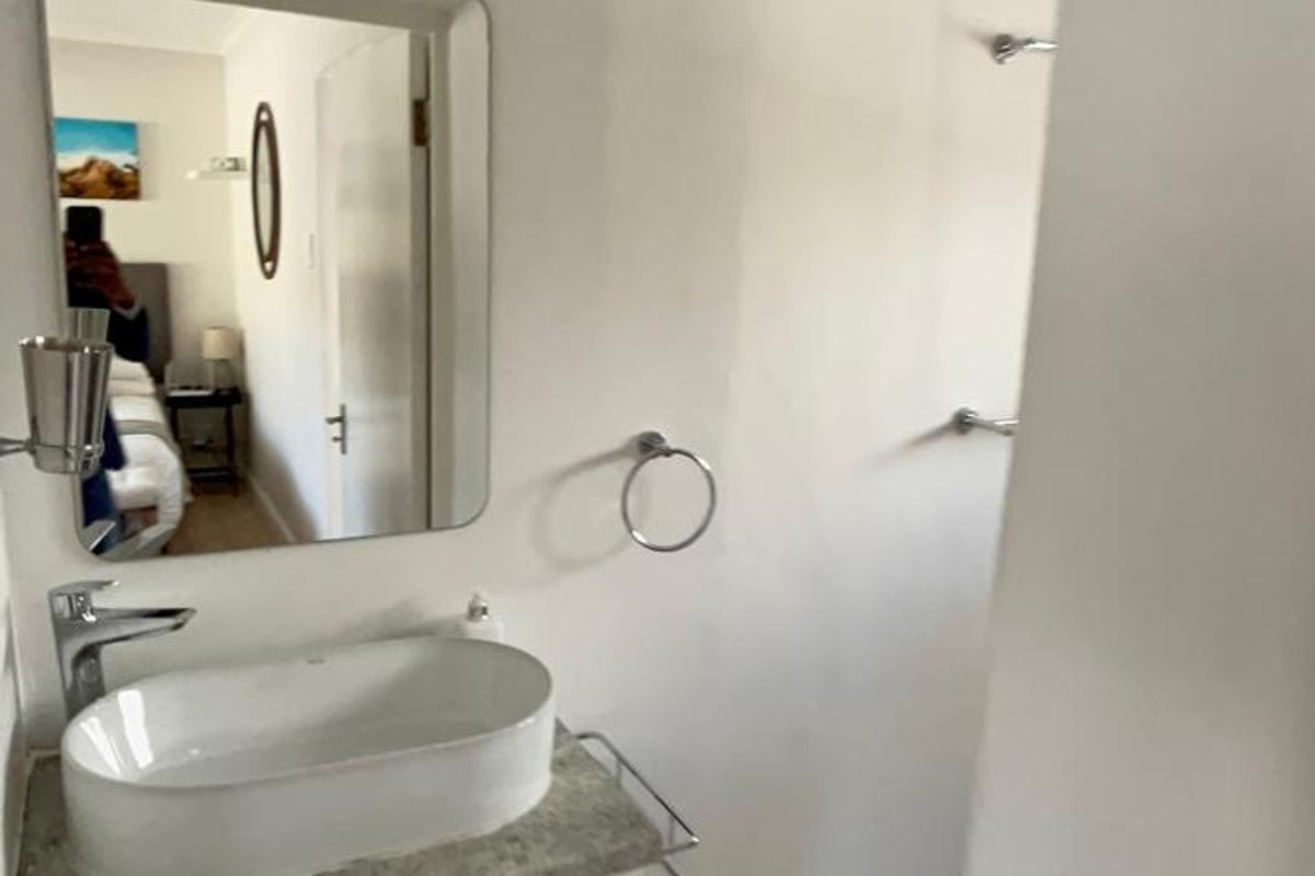 A functional bathroom featuring a modern vessel sink on a vanity cabinet, wall-mounted mirror, and a walk-in shower area with tiled flooring.