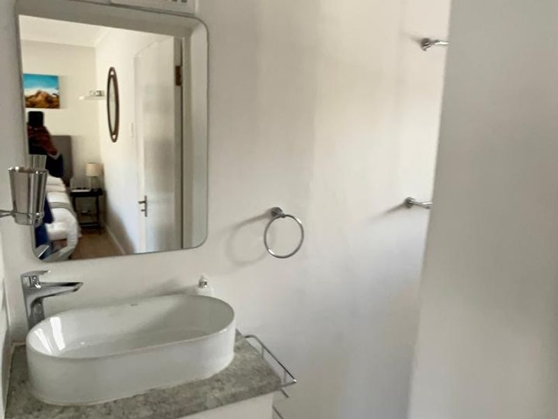 A functional bathroom featuring a modern vessel sink on a vanity cabinet, wall-mounted mirror, and a walk-in shower area with tiled flooring.