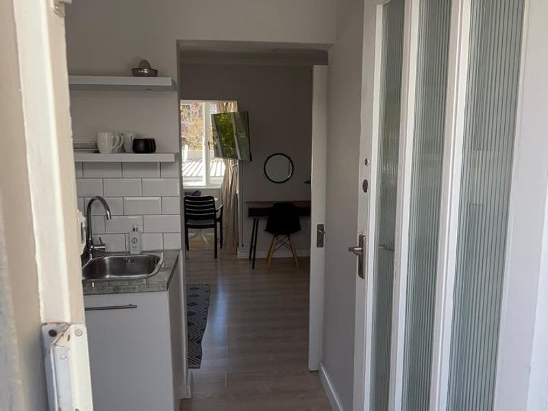 Entryway leading into a compact kitchenette area featuring a stainless steel sink, subway tile backsplash, and modern laminate flooring.