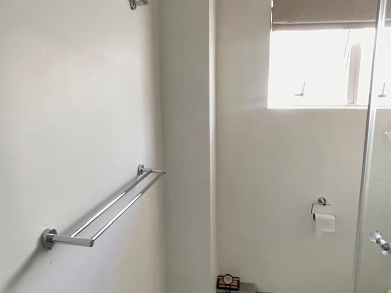 A functional bathroom featuring tiled flooring, a glass shower screen, and wall-mounted towel rails.