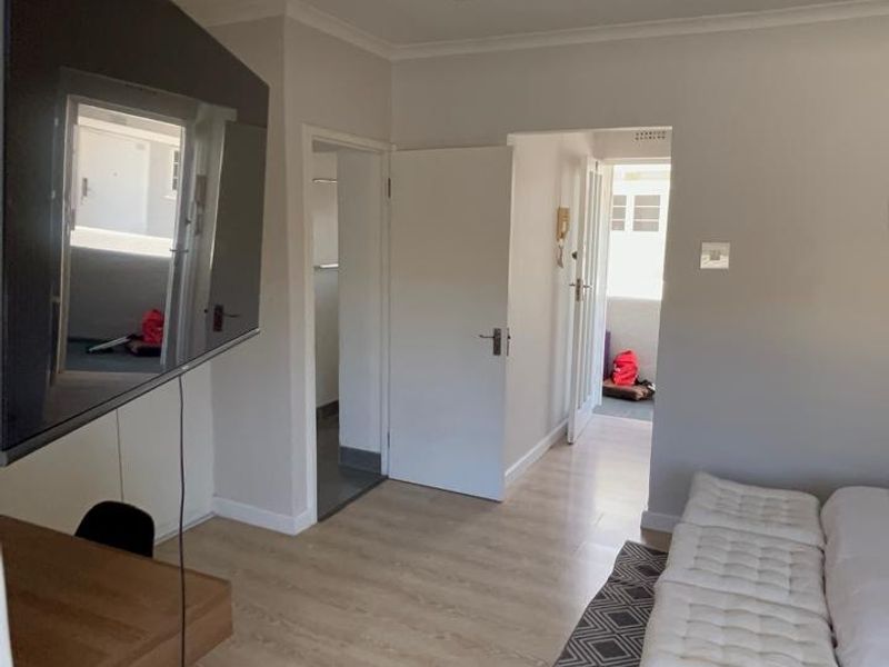 A well-maintained bedroom featuring light laminate flooring, neutral walls, and access to an adjoining bathroom and balcony area.