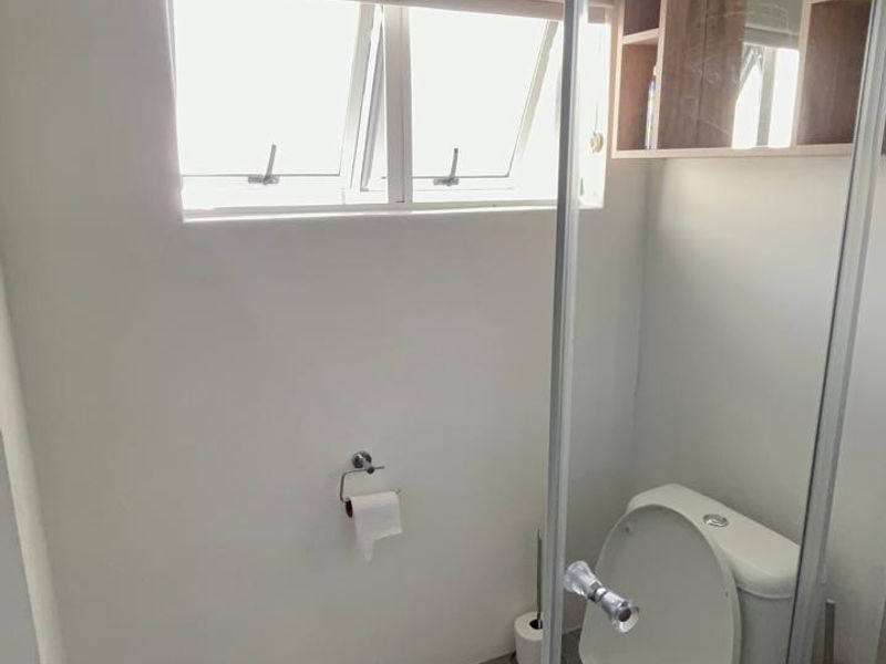 A compact bathroom featuring a modern toilet, glass shower screen, and built-in wall shelving with neutral tiled flooring.