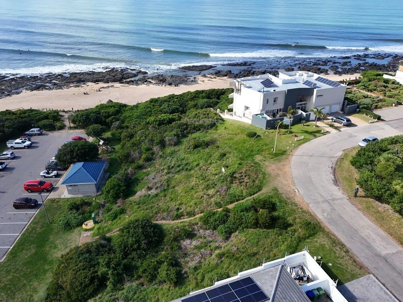 Aerial view of a vacant residential plot situated in a prime coastal location, featuring direct proximity to the beach and established road access.