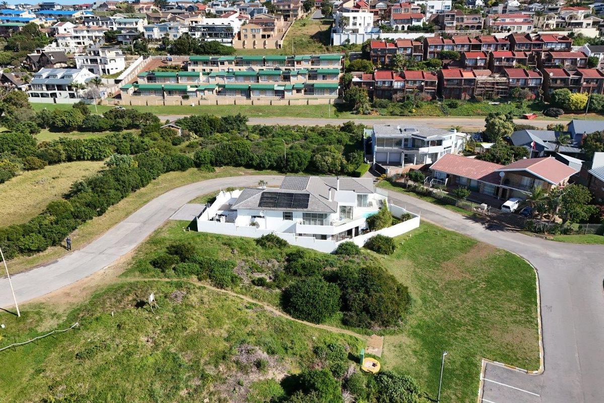 Aerial view of a residential property featuring a tiled roof with solar panels, surrounded by a boundary wall and paved driveway in a suburban setting.