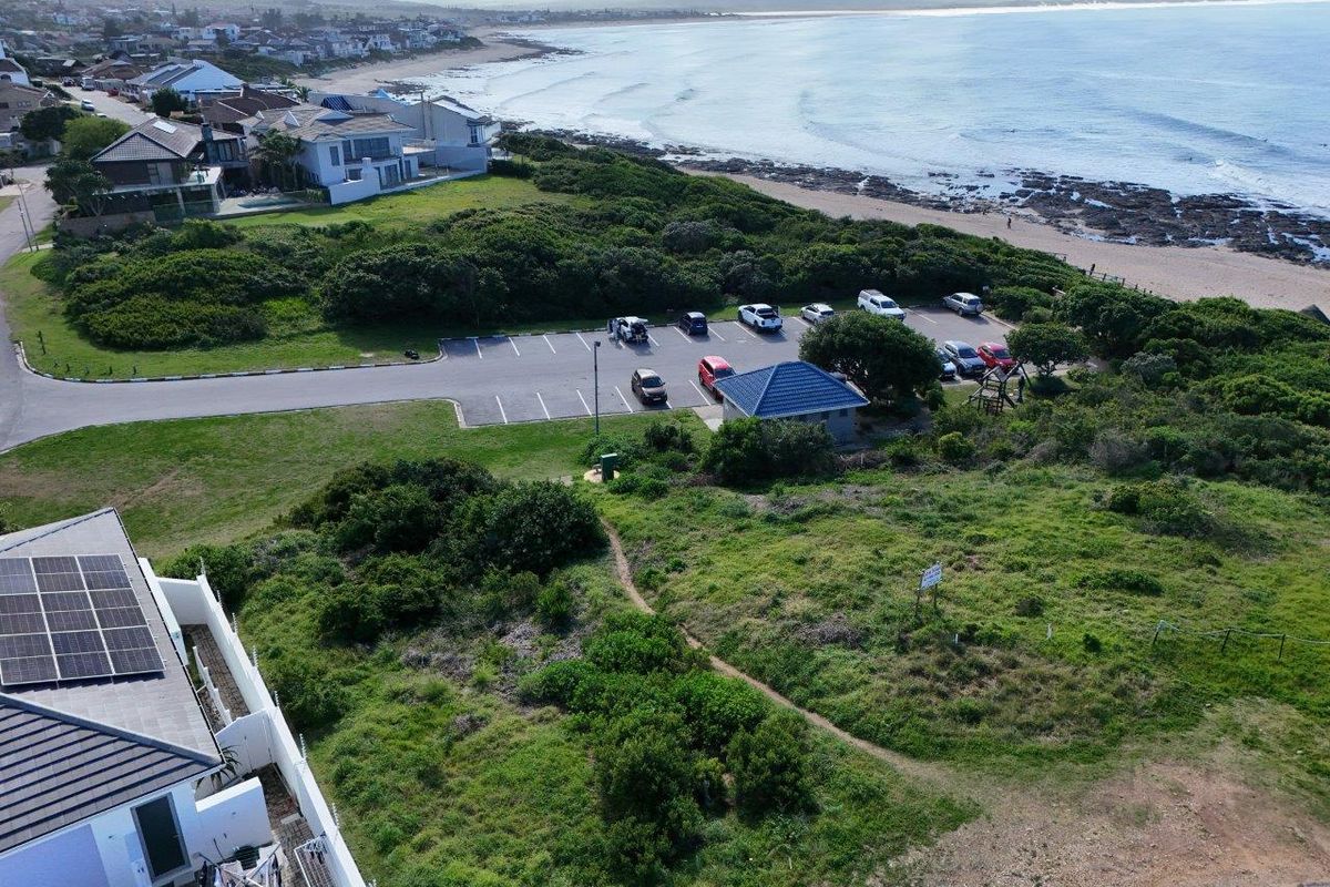 Aerial view of the coastal residential property, showcasing proximity to the beach, public parking area, and existing solar panel installation.
