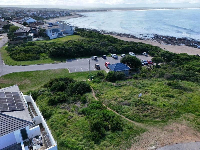 Aerial view of the coastal residential property, showcasing proximity to the beach, public parking area, and existing solar panel installation.