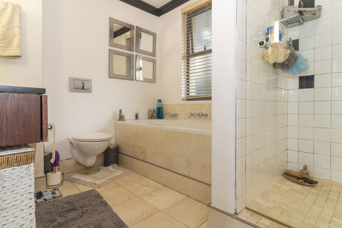 A functional bathroom featuring a wall-mounted toilet, a built-in bathtub, and a separate glass-enclosed shower with tiled finishes.