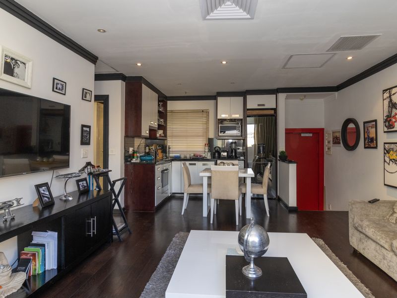 Open-plan living and dining area featuring dark wood flooring, recessed lighting, and a compact kitchen with built-in cabinetry and integrated appliances.