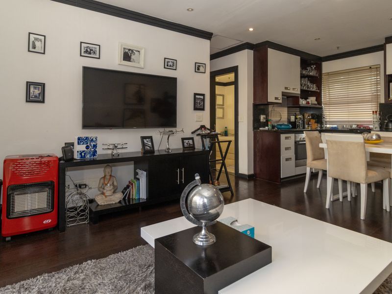 An open-plan living and dining area featuring dark laminate flooring, modern cabinetry, and recessed lighting, creating a functional and cohesive apartment living space.