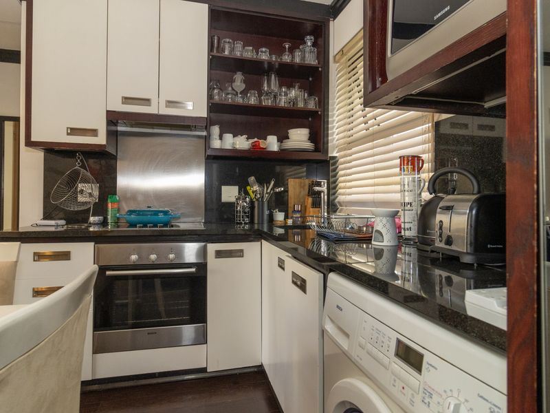 Compact kitchen featuring granite countertops, built-in oven, electric hob, stainless steel splashback, and ample cabinetry with integrated microwave.