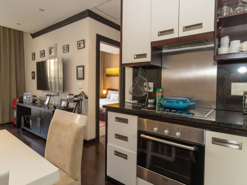 Open-plan living area featuring a compact, modern kitchen with built-in appliances, granite countertops, and dark wood flooring, seamlessly connected to the living space.