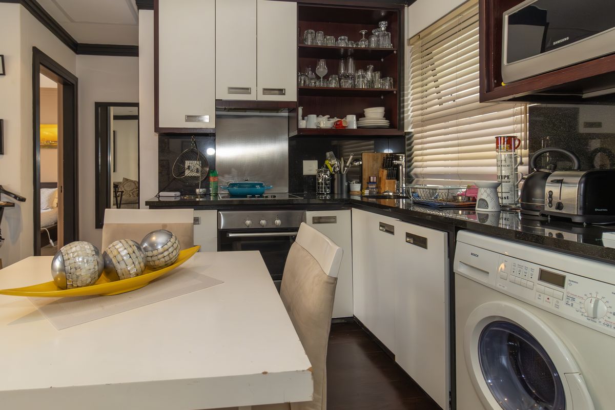 Compact kitchen featuring modern white cabinetry, granite countertops, integrated appliances, and a stainless steel splashback, offering a functional and efficient cooking space.