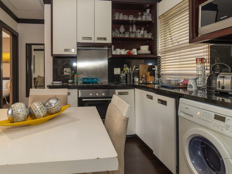 Compact kitchen featuring modern white cabinetry, granite countertops, integrated appliances, and a stainless steel splashback, offering a functional and efficient cooking space.