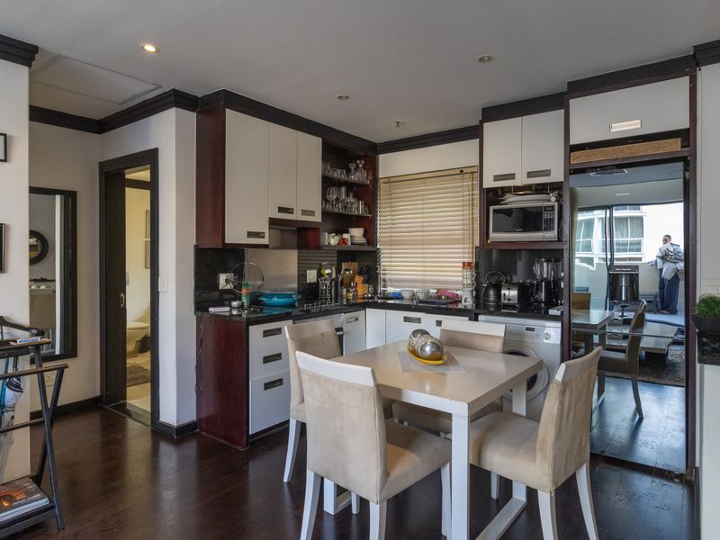 Open-plan kitchen and dining area featuring dark wood cabinetry, integrated appliances, and dark laminate flooring, leading to an adjacent balcony.
