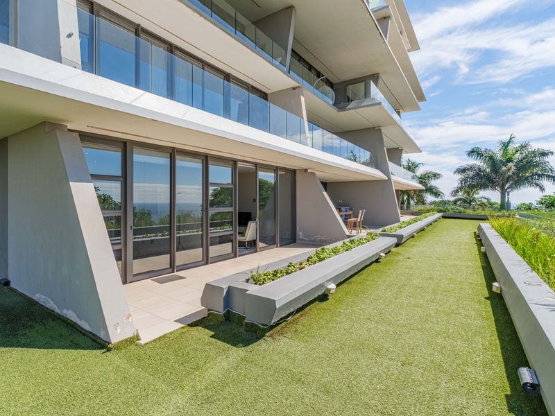 Spacious ground-floor patio featuring artificial turf, built-in concrete planters, glass balustrades, and large sliding doors providing seamless indoor-outdoor flow.