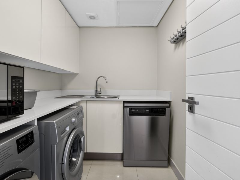 A modern, well-maintained laundry room featuring sleek built-in cabinetry, stone countertops, a stainless steel sink, and space for integrated appliances.