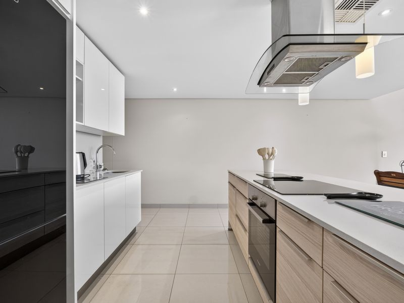 Modern kitchen featuring sleek white cabinetry, light wood-toned island, stone countertops, integrated appliances, and high-quality finishes throughout.