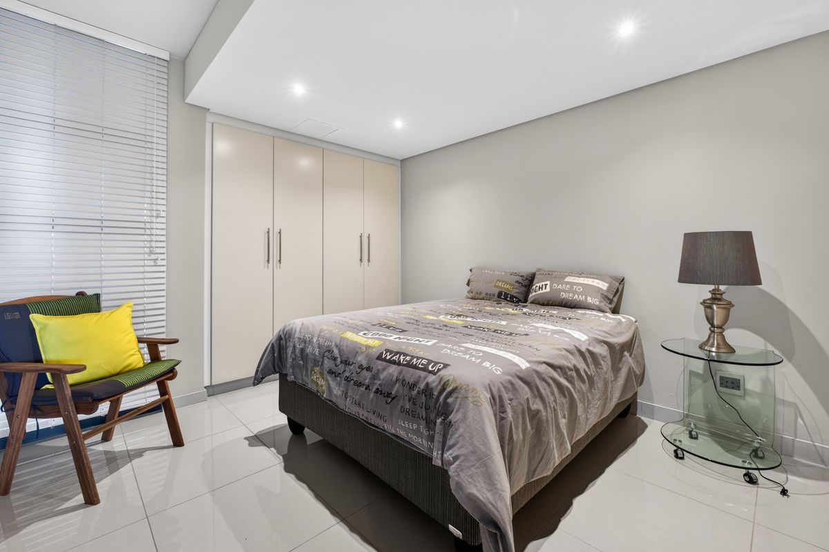 A well-maintained bedroom featuring neutral tiled flooring, recessed downlighting, and a large built-in wardrobe with modern cabinetry.