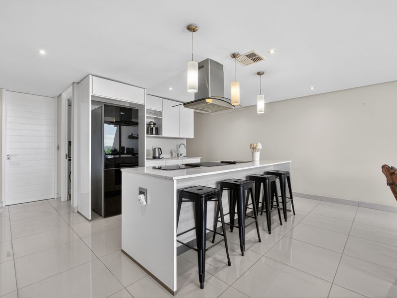 Modern kitchen featuring a central island with integrated hob, sleek white cabinetry, stainless steel extractor fan, and polished tiled flooring.