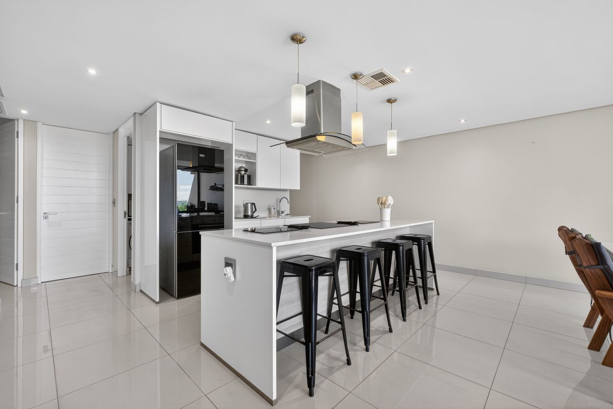 Modern kitchen featuring a central island with integrated hob, sleek white cabinetry, stainless steel extractor fan, and polished tiled flooring.
