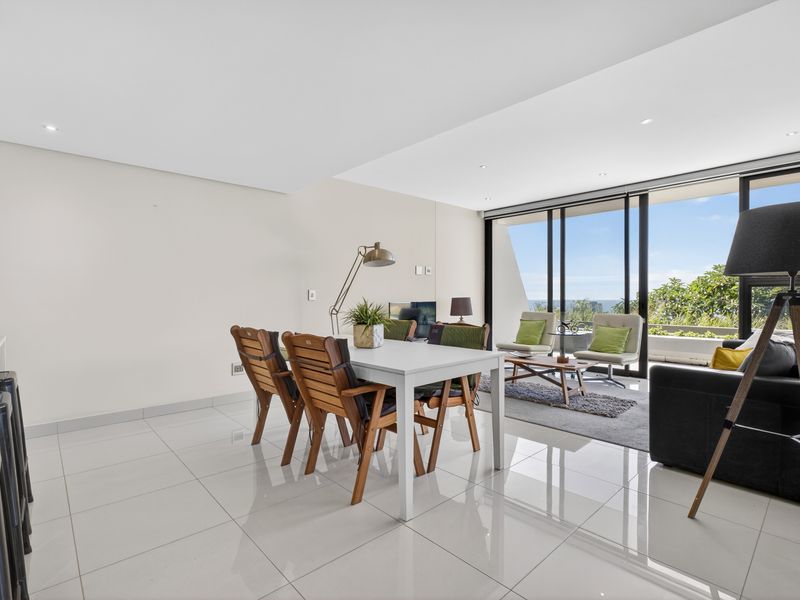 Spacious open-plan living and dining area featuring sleek porcelain floor tiles, recessed lighting, and large sliding glass doors leading to an outdoor balcony.