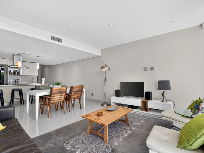 Spacious open-plan living and dining area featuring modern porcelain tiling, recessed lighting, and a sleek kitchen with integrated cabinetry and island.