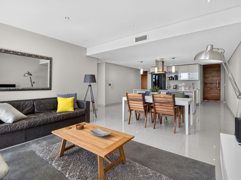 Spacious open-plan living and dining area featuring glossy tiled floors, recessed lighting, and a modern kitchen with a central island and built-in cabinetry.