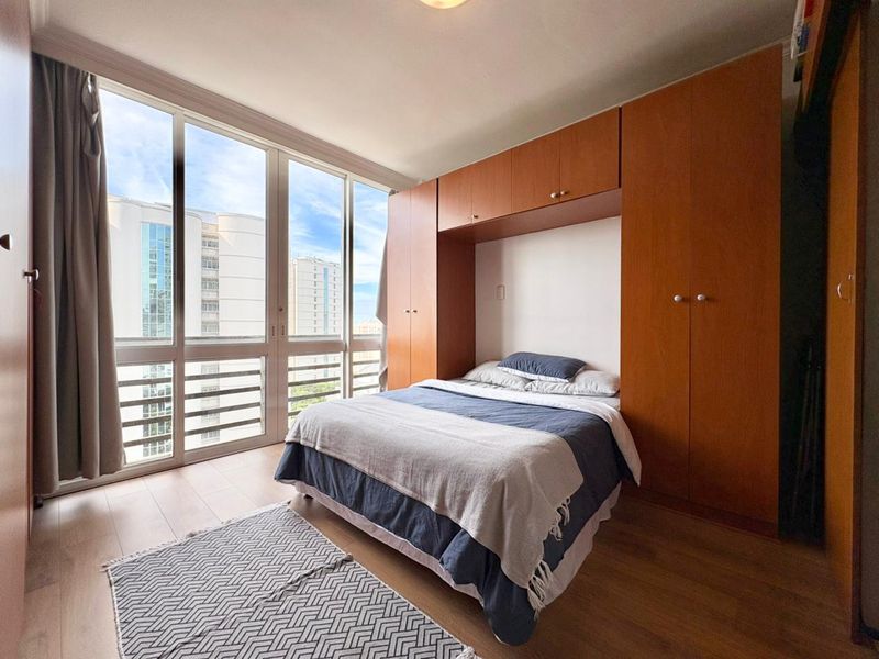 A bright bedroom featuring floor-to-ceiling windows with city views and extensive built-in wooden cabinetry for storage.