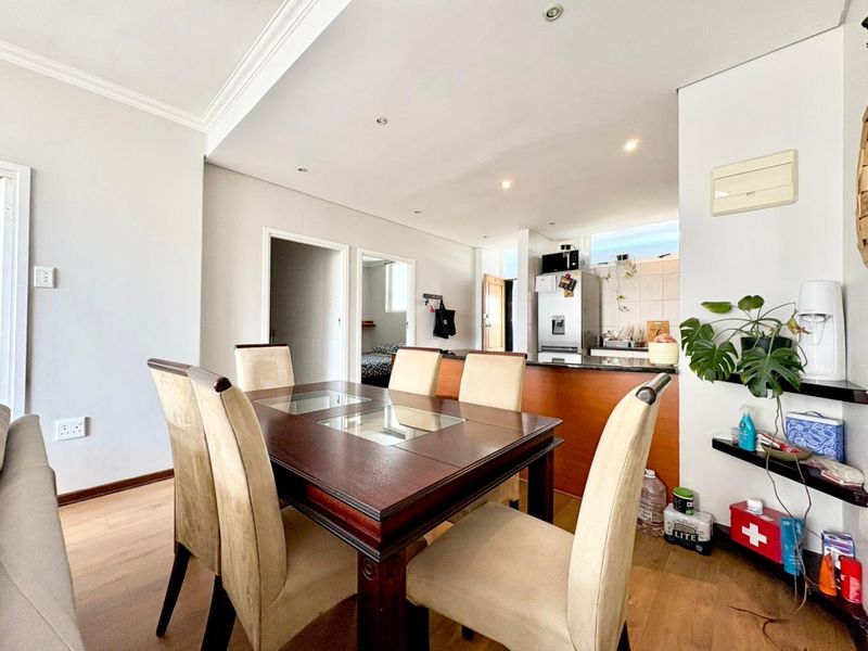 Open-plan dining area featuring laminate flooring and recessed lighting, seamlessly flowing into a functional kitchen with granite countertops and built-in cabinetry.