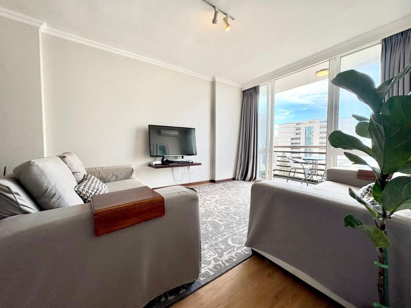 A bright living room featuring laminate flooring, track lighting, and a large sliding glass door providing access to a private balcony.