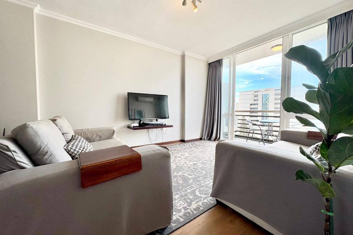 A bright living room featuring laminate flooring, track lighting, and a large sliding glass door providing access to a private balcony.